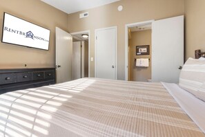 Habitación de hotel con cama, cómoda, televisor de pared mostrando RENTBRINS.COM y baño con toallero y retrete.