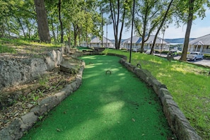 Un campo de croquet verde con bordes de piedra, rodeado de árboles y vistas de edificios al fondo.