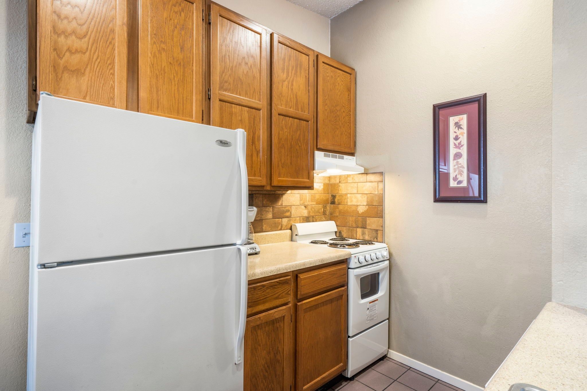 A compact kitchen with wooden cabinets, a white refrigerator, a stove, and a countertop.