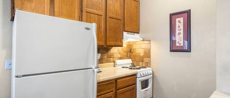 A compact kitchen with wooden cabinets, a white refrigerator, a stove, and a countertop.