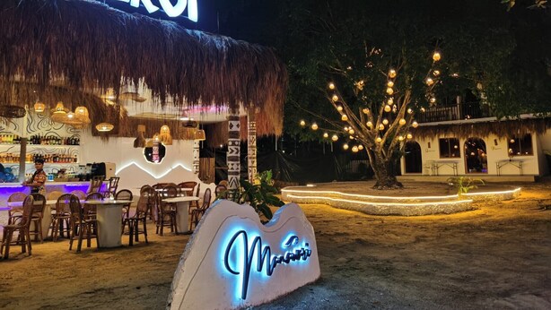 Un café frente al mar llamado 'Cafe ELROI' con mesas al aire libre y techo de paja.