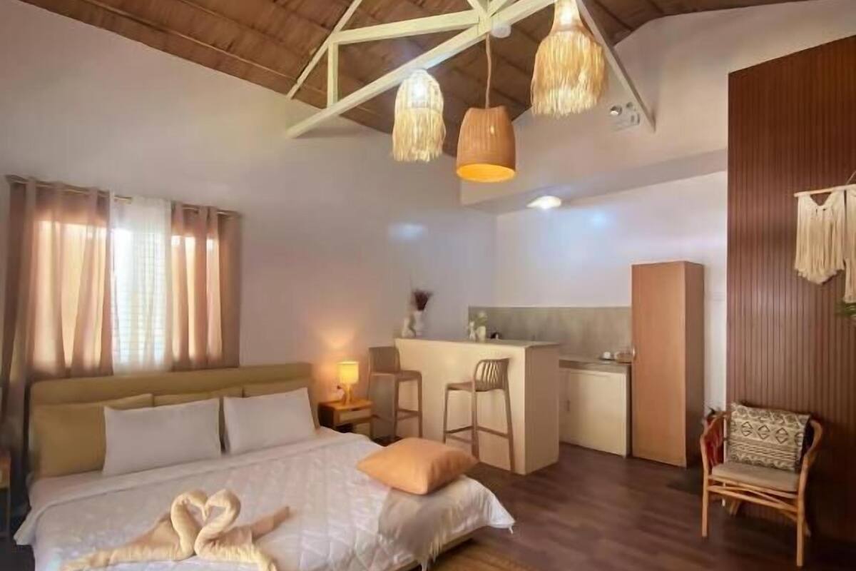 A bedroom with a bed, a woven rug, a desk, and a chair.