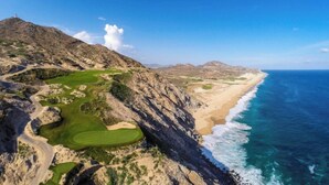 A coastal landscape with a golf course, a lighthouse, and a beach.