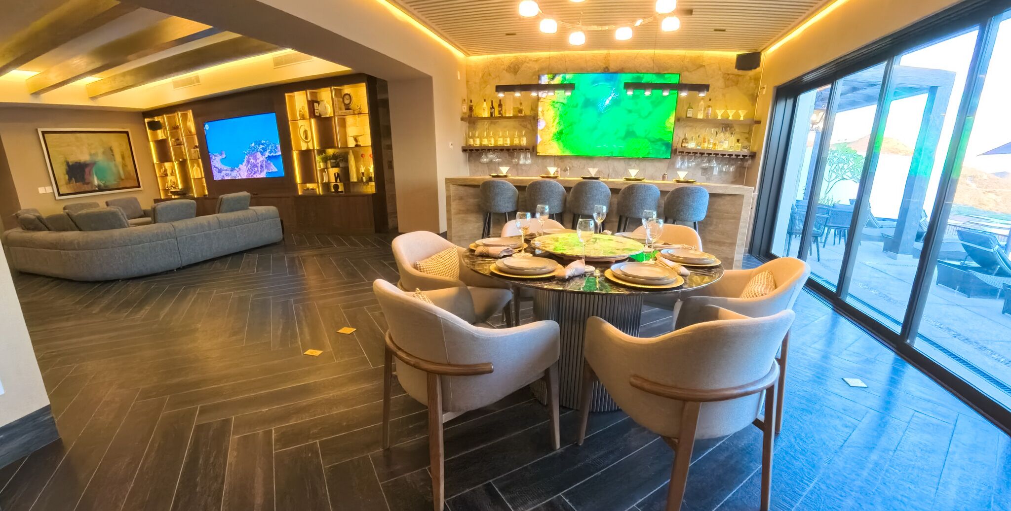 A modern dining area with a large table set for six, a bar with a TV, and a cozy seating area with a sofa and chairs.