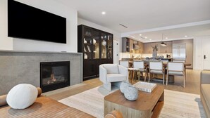 A modern living room with a fireplace, a flat-screen TV, and a dining area with a kitchen in the background.