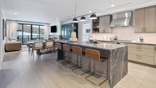 A modern kitchen with a central island, bar stools, and a dining area with a sofa and table.