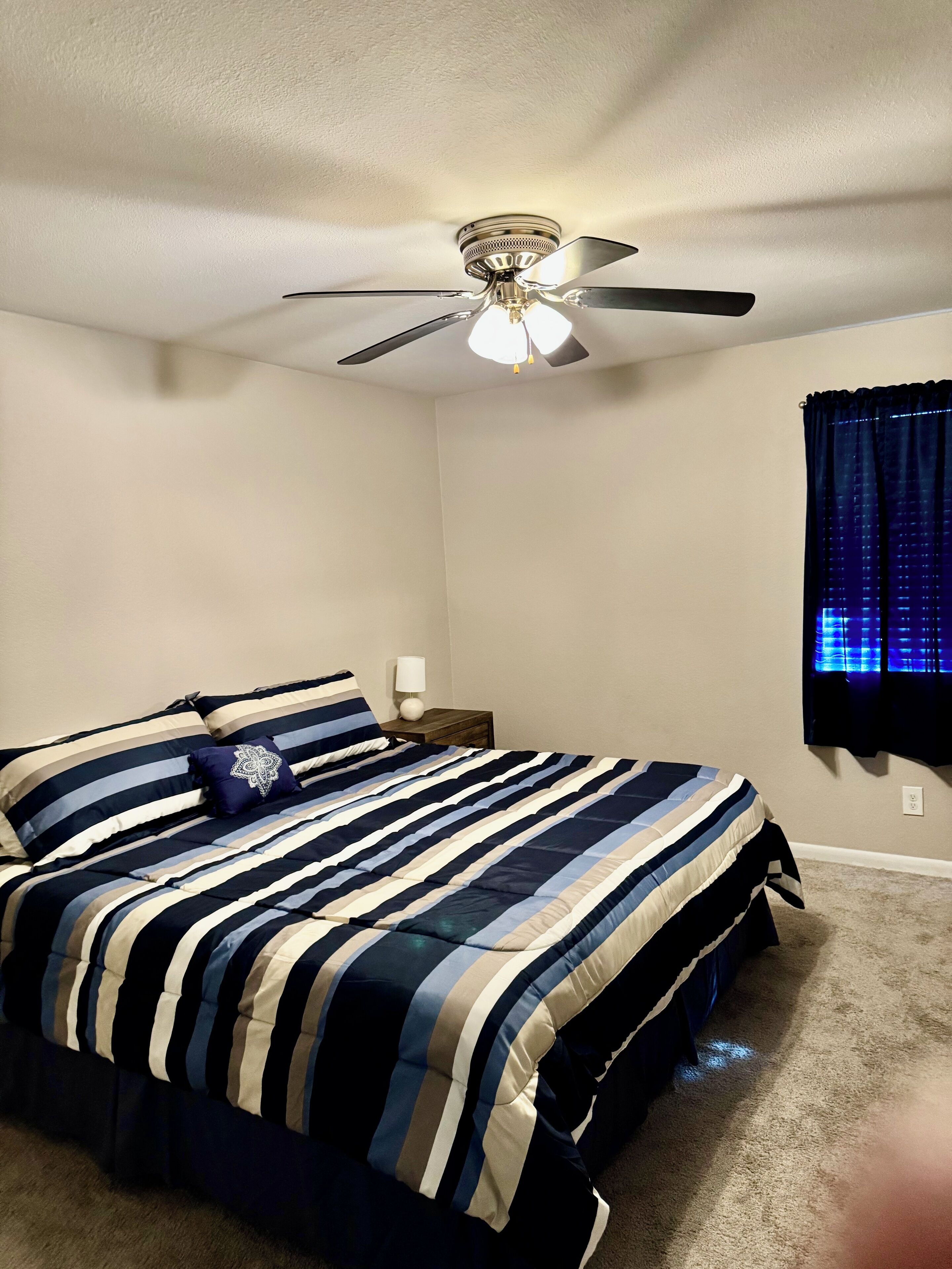 A bedroom with a bed, a ceiling fan, a nightstand, and a window with curtains.