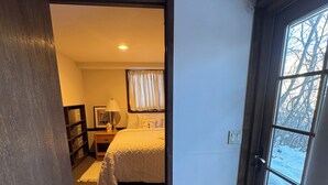 A hotel room with a bed, a nightstand, a lamp, a window with a view of trees, and a door leading to another room. - Pet friendly 1 bedroom, in the heart of Snowmass Vlg (Snowmass Village)