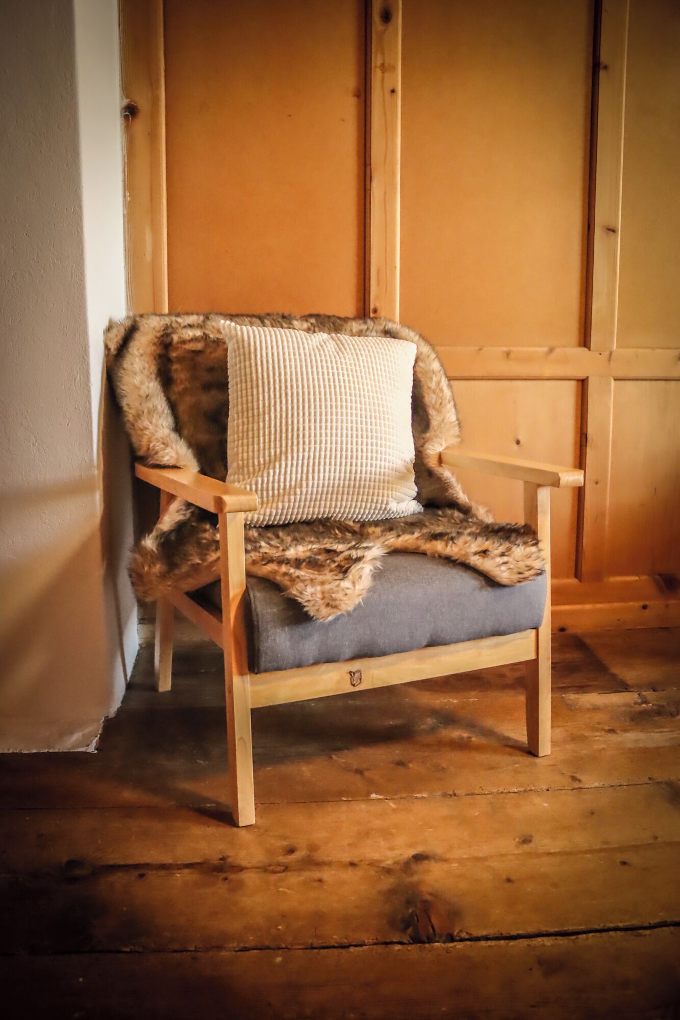 A wooden chair with a fur throw and a checkered pillow.