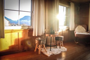 A cozy room with wooden walls, a wooden floor, a window with a mountain view, a small table with a vase and cup, and a fluffy chair. - Quaint vacation home in the mountains - pure relaxation and nature! (Lingenau)