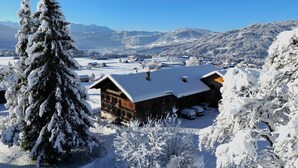 A snow-covered lodge with a wooden exterior, multiple windows, and a snow-covered roof. - Quaint vacation home in the mountains - pure relaxation and nature! (Lingenau)