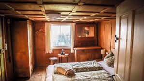 A wooden cabin bedroom with a bed, a small table, and a window. - Quaint vacation home in the mountains - pure relaxation and nature! (Lingenau)