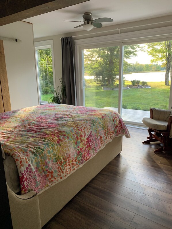 Ein Schlafzimmer mit einem großen Bett, einem Deckenventilator und Seeblick durch große Fenster.