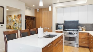 A modern kitchen with a central island, stainless steel appliances, wooden cabinets, and a large painting on the wall.