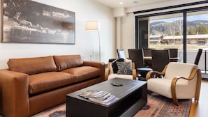A modern living room with a brown leather sofa, a black coffee table with magazines, a white armchair, and a large painting of wildlife on the wall.