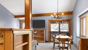 Un coin repas avec une table et des chaises en bois, un lustre et un téléviseur fixé au mur.