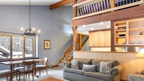 Un salon chaleureux avec un canapé, une table basse et un escalier menant à une mezzanine aménagée en bibliothèque.
