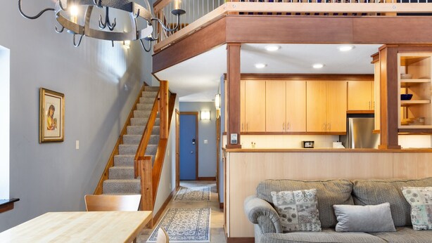Un intérieur moderne avec un escalier menant à une mezzanine, un coin repas et une cuisine dotée de meubles en bois.