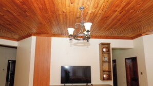 Una habitació amb sostre de fusta, un televisor de pantalla plana muntat sobre una estant de fusta i una làmpada penjant.
