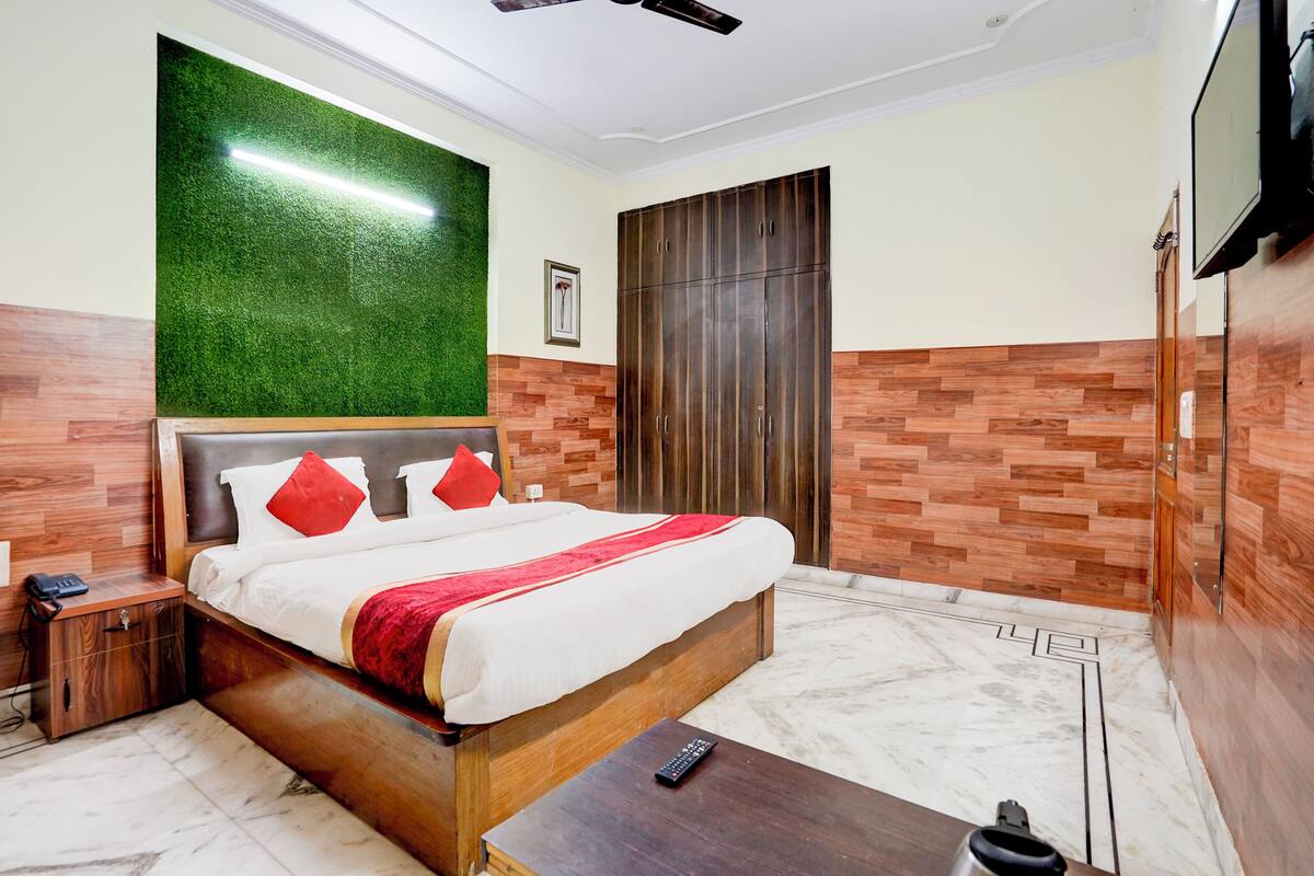 A hotel room with a bed, a nightstand, a wooden bench, a TV, and a wardrobe.