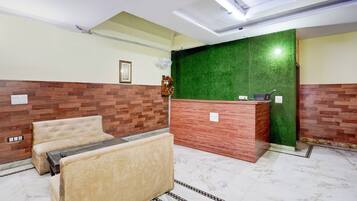 Un hall d’hôtel comprenant un comptoir d’accueil, un espace détente avec un canapé et des fauteuils, et un mur végétal.