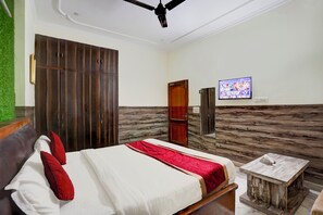 A hotel room with a bed, a wooden wardrobe, a television, and a small table.