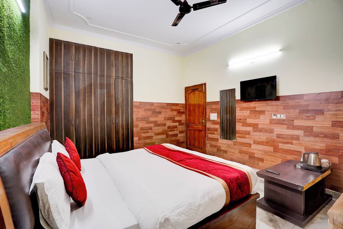 A hotel room with a bed, a wardrobe, a television, and a small table with a kettle.