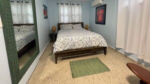 A bedroom with a bed, a mirror, a window with curtains, an air conditioner, and a framed picture on the wall.