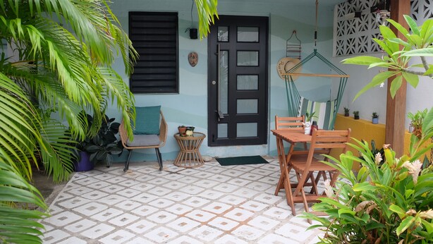 A patio with a tiled floor, a wooden table and chairs, potted plants, and a door with a window.