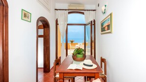 Un comedor con una mesa, sillas, una planta y vista al mar.