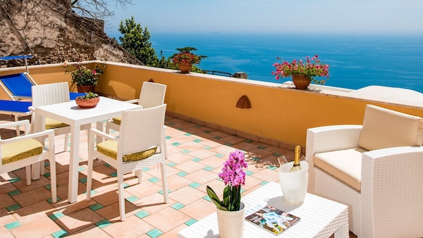 Una terraza con muebles de mimbre blanco, una mesa con un florero y vistas al mar.