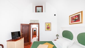 Un dormitorio con una cama, un televisor sobre un mueble, y una puerta que da a otra habitación.