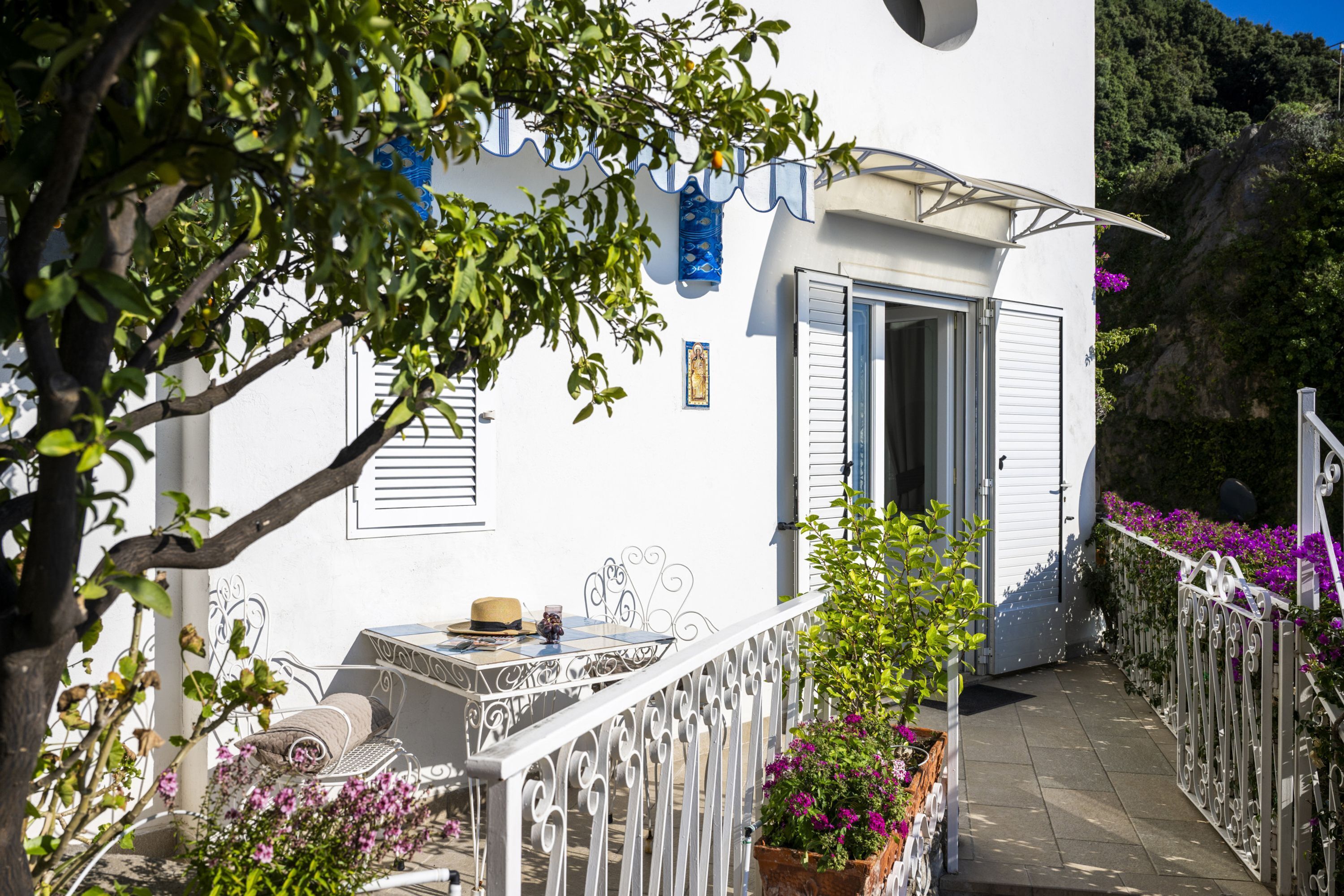 A white building with a balcony, a table with a hat, and a chair.