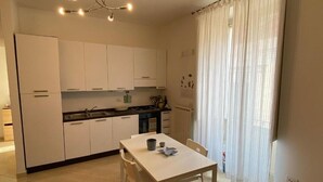 A modern kitchen with white cabinets, a dining table, and a window with sheer curtains.