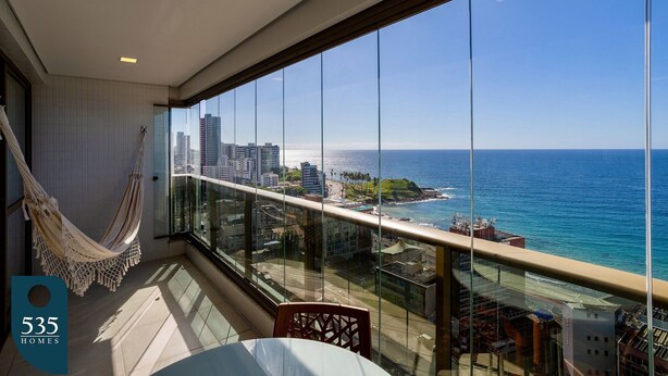 Un balcon avec vue sur l’océan et la ville, un hamac et une table avec des chaises.