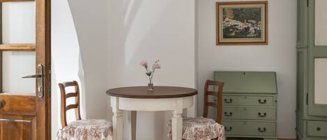 A room with a bed, a wooden chair, a small table with a vase, and a green dresser.