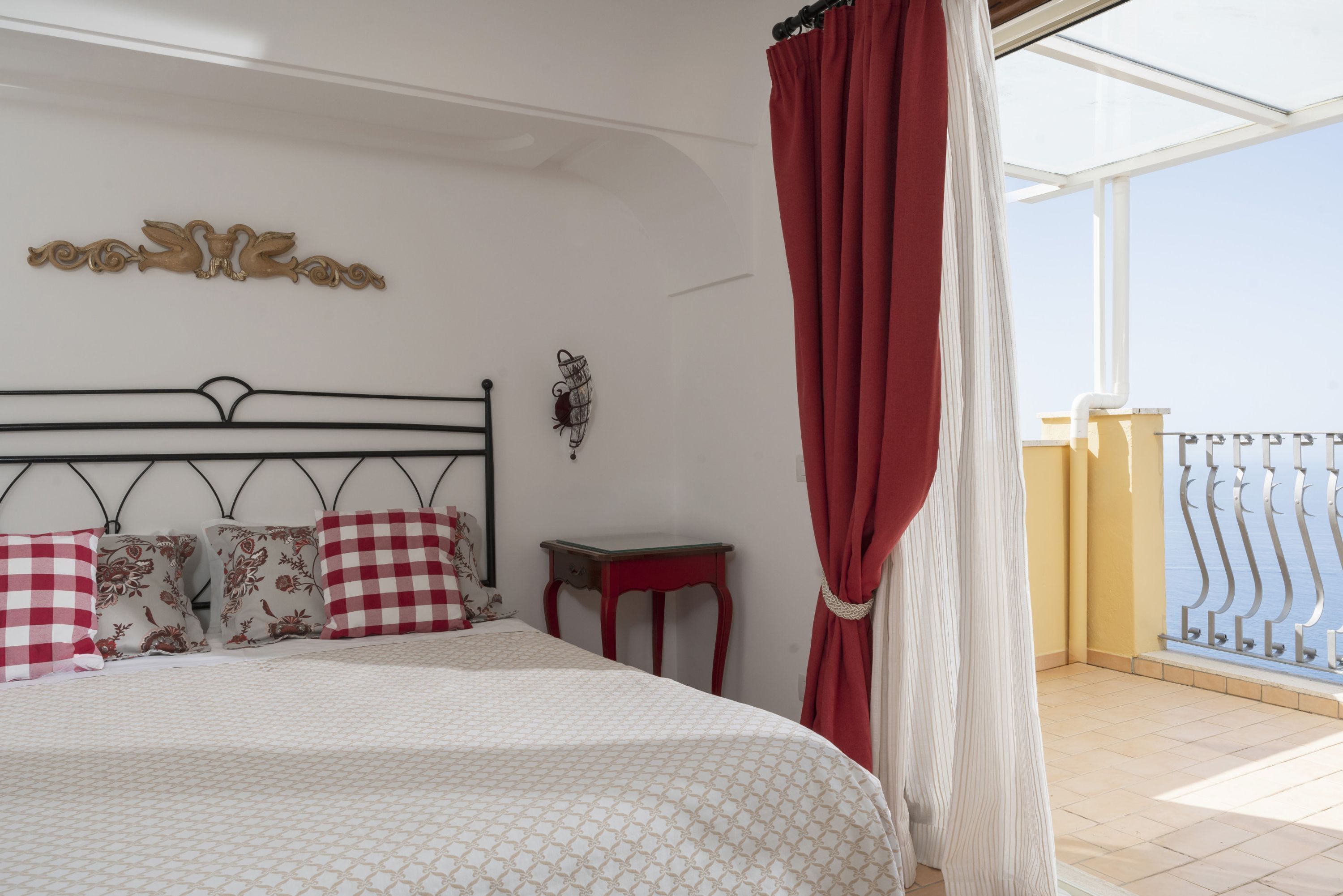 A bedroom with a bed, pillows, a bedside table, a decorative wall piece, and a balcony with a railing.