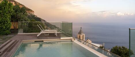 Een dakzwembad met oneindige horizon, een glazen balustrade, een ligstoel en uitzicht op de oceaan.