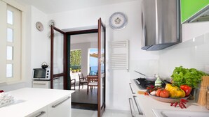 A modern kitchen with white cabinets, a stainless steel range hood, and a dining area with a view of the sea. - Villa Mapi in Massa Lubrense (Massa Lubrense)