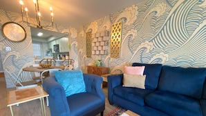 Un salon avec un canapé bleu, un fauteuil bleu et une table basse. Un mur à motifs et un lustre décorent la pièce.