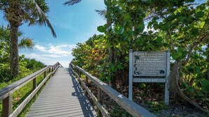 Une promenade en bois menant à une plage, avec un panneau d’information.