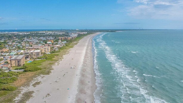 Un paysage urbain côtier avec une longue plage, des bâtiments et un ciel dégagé.
