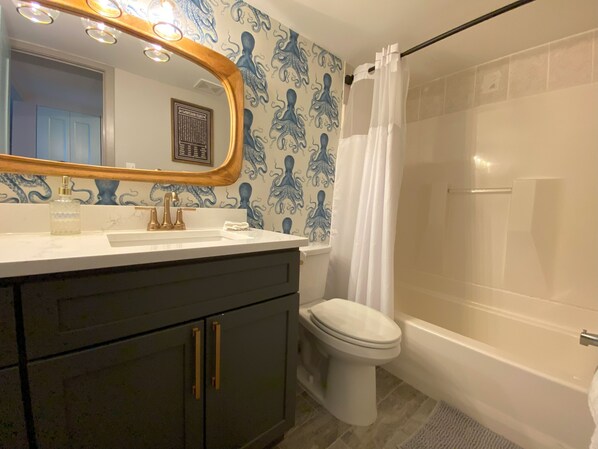 Un baño con lavamanos blanco, inodoro y ducha con cortina blanca.
