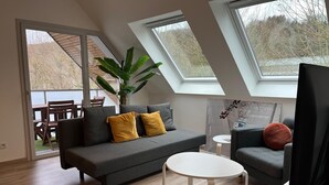 En moderne stue med en grå sofa, et rundt hvidt bord og en potteplante.