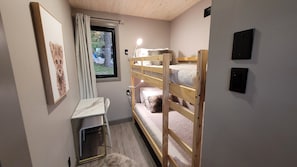 Une chambre avec un lit superposé, un petit bureau et une chaise, une fenêtre avec des rideaux et un tableau encadré au mur.
