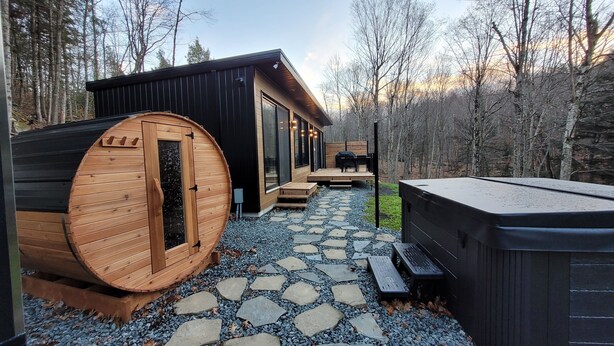 Un sauna avec une structure extérieure en bois, un espace patio avec des meubles d’extérieur et un jacuzzi.