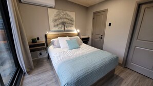 Une chambre à coucher comprenant un lit, des tables de chevet, une commode, un tableau accroché au mur et une porte.