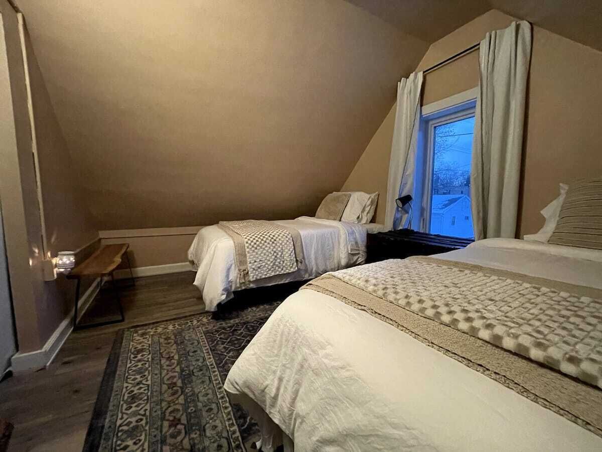 Una camera da letto con due letti, una finestra con tende, una panca di legno e un tappeto decorato.