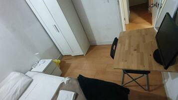 Habitación pequeña con cama, un escritorio, una silla y televisor. Hay una puerta que conduce a otra habitación.
