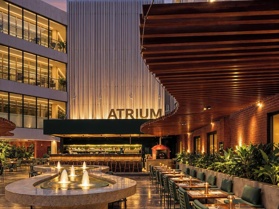 Ein Außenbereich zum Essen mit einer Bar, einem Brunnen und einem Gebäude mit der Aufschrift 'ATRIUM'.